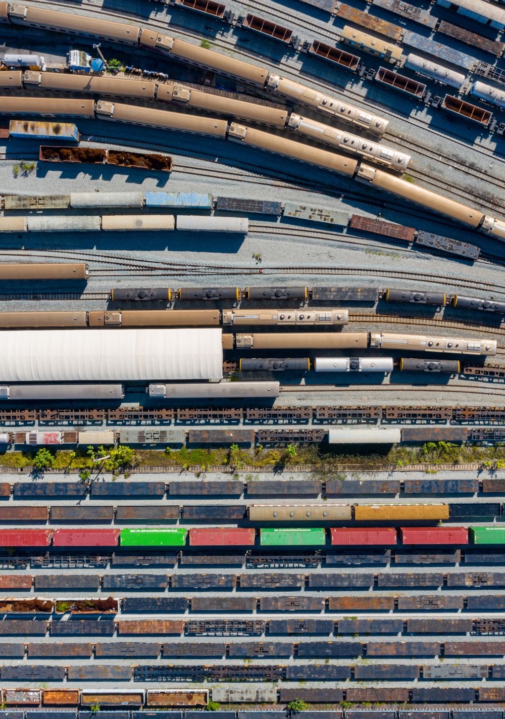 Top-down drone image of freight containers aligned in symmetrical pattern at rail terminal, reflecting modern transport system and commercial organization.